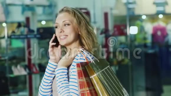 一个有魅力的女人带着购物袋在电话里说话它是在玻璃陈列柜的背景下视频的预览图
