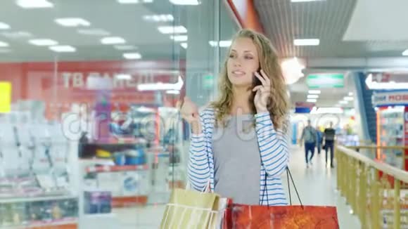 一个有魅力的女人拿着购物袋走在商场里用手机说话视频的预览图