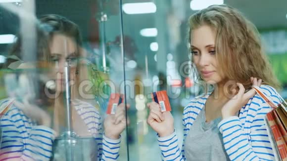 漂亮的年轻女人看着商店里的一个玻璃陈列柜手拿着购物卡和视频的预览图