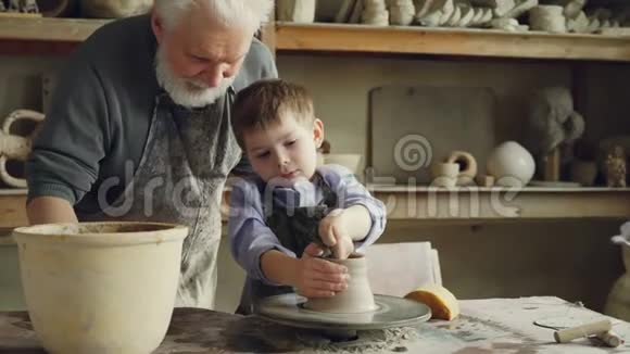 专心致志的小男孩正在学习用粘土在传统车间的陶器课上投掷轮他的视频的预览图