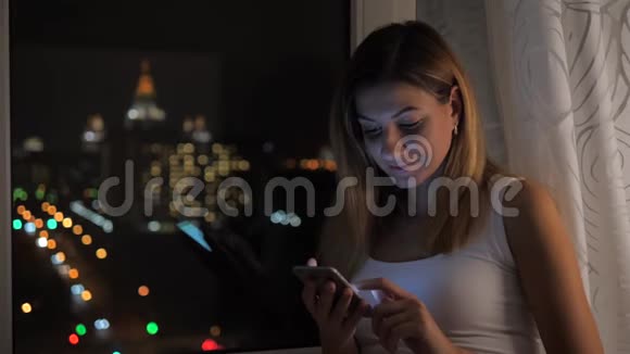 站在窗前看夜景的美女使用智能手机视频的预览图