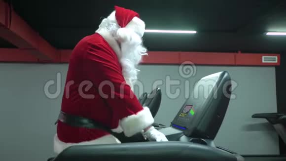 圣诞老人在健身房训练圣诞节圣诞老人在健身俱乐部的跑步机上跑步视频的预览图