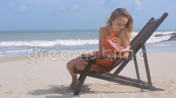 金发女郎坐在甲板椅上海滩上有日记视频的预览图