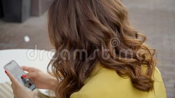 穿黄色衣服的女孩在咖啡馆的露台上使用智能手机视频的预览图