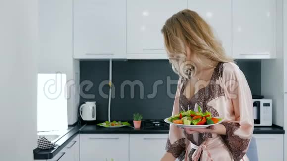 早上好穿丝绸睡衣的快乐女人拿着蔬菜沙拉和玻璃杯里的水视频的预览图
