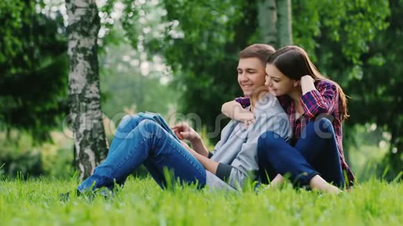年轻夫妇男女坐在公园的草地上享受石碑女孩压在男人身上视频的预览图