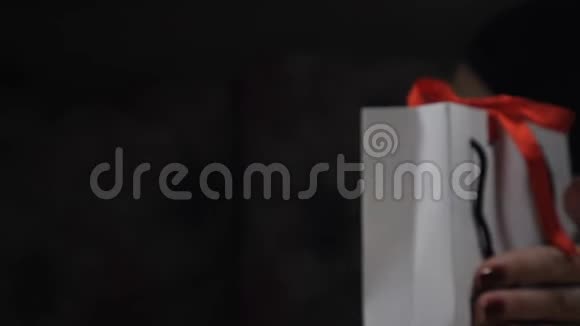 女性手指的特写展示了带有红色丝带和蝴蝶结的纸礼盒以女人的身份打开一个礼品盒视频的预览图