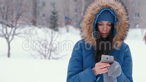 冬天降雪时年轻漂亮的女人在户外打电话视频的预览图