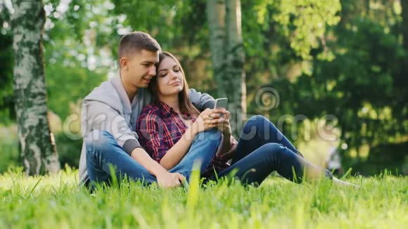 年轻夫妇一起在公园里休息玩你的电话微笑视频的预览图