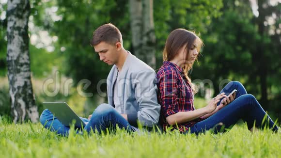 年轻人在大自然中休息男人用笔记本电脑女孩用自拍智能手机视频的预览图