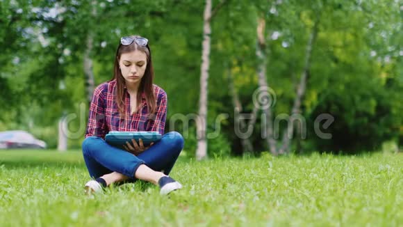 一名女学生正在准备考试坐在公园的草坪上享受平板电脑视频的预览图