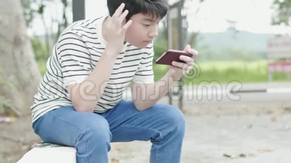 亚洲十几岁的男孩在路边玩手机游戏视频的预览图