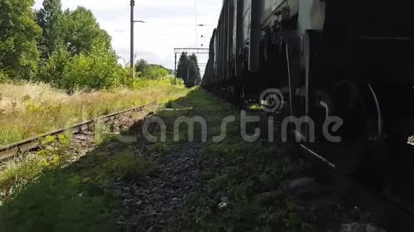 在货运列车底盘附近的旧火车站4K走在长满草的车辙上视频的预览图