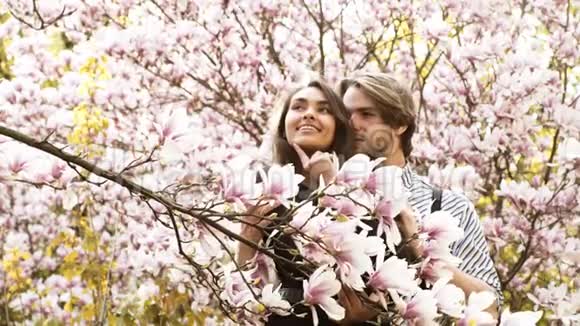 年轻美丽幸福的微笑夫妇在开花树旁摆姿势视频的预览图