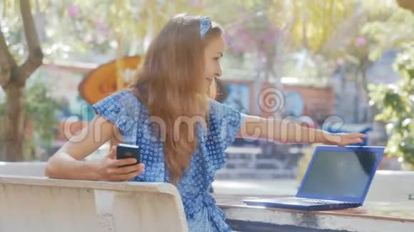 坐在长凳上的蓝衣少女将笔记本电脑夹在桌面上视频的预览图