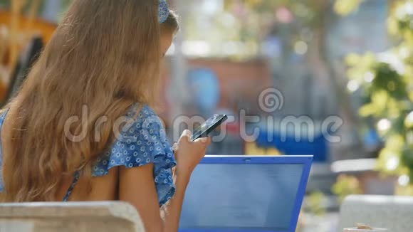 穿蓝色衣服的金发女孩在公园看智能手机视频的预览图