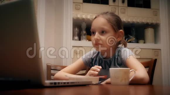 伤心的女孩吃零食看着厨房的桌子上的笔记本电脑屏幕视频的预览图