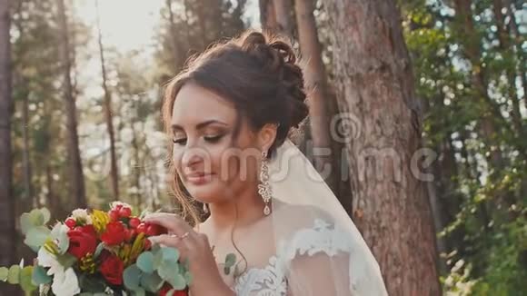 迷人而快乐的新娘穿着一件漂亮的婚纱在阳光下的松林里放着一束鲜花婚礼日视频的预览图