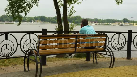 男人打电话在公园长椅上放松看着城市河流周末休息视频的预览图