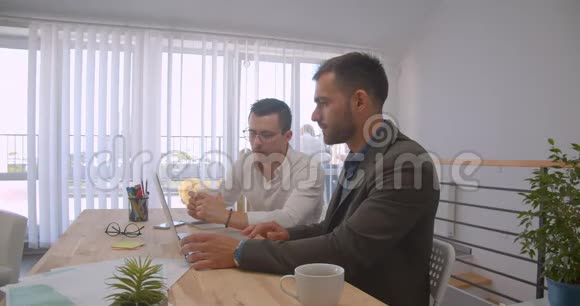 两个成年白种人商人使用笔记本电脑和在办公室在室内交谈的画像视频的预览图