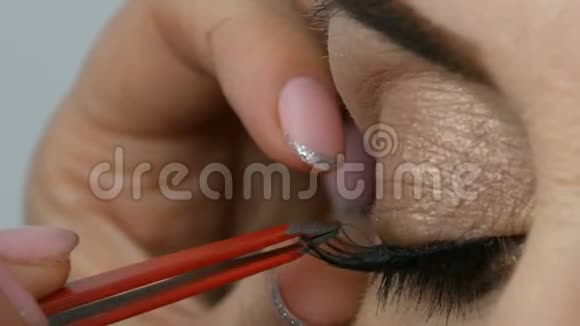 专业化妆师把假睫毛贴在一个成年中年妇女的蓝色眼睛上近距离观看视频的预览图