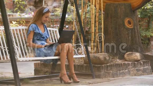 金发女郎坐在长凳上在公园里摆着平板视频的预览图