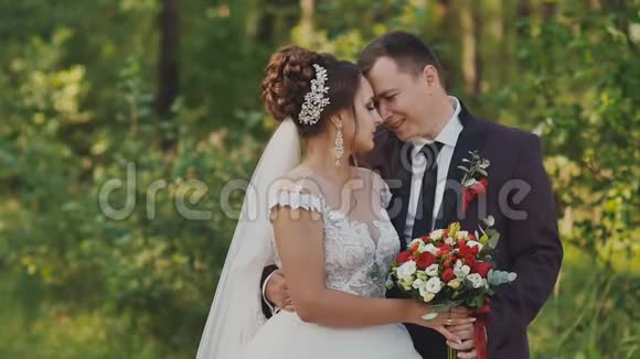 新郎新娘带着花束在森林里新郎拥抱他的新娘一个温柔的吻一起快乐在这一刻视频的预览图