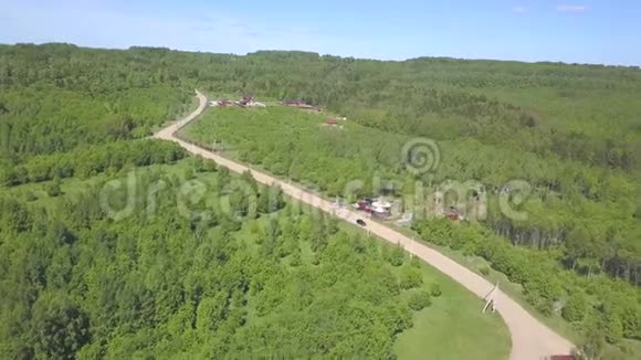 汽车在乡间道路上行驶的鸟瞰图靠近草地和森林环绕的农舍有针叶树和针叶树视频的预览图