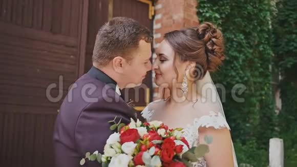 新娘和新郎手里拿着一束明亮的花手里拿着一堵砖墙墙上长着葡萄枝快乐视频的预览图