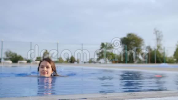 年轻女性在游泳池户外饮用有色饮料的积极姿态视频的预览图