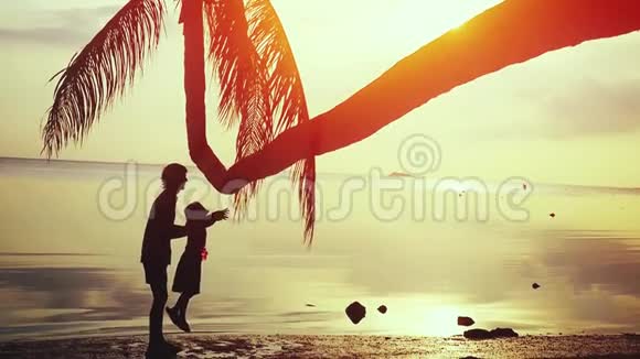 年轻快乐的父亲和他的女儿在棕榈树的背景下惊人的日落慢动作视频的预览图