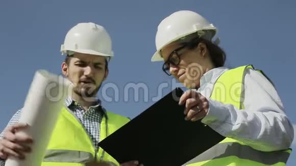 两个年轻的工程师一个男人和一个女人在绿色的背心和头盔视频的预览图