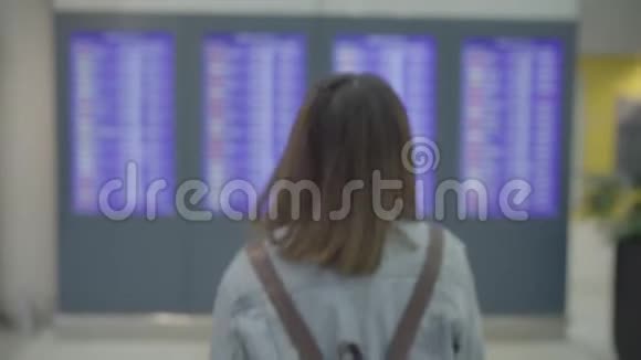 快乐的亚洲女人看着信息板在登机口的候机大厅里拿着行李检查她的航班视频的预览图