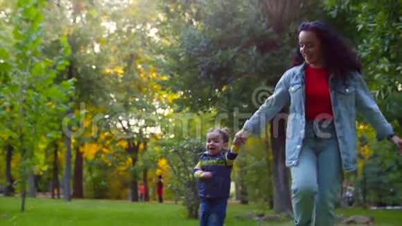 幸福家庭的概念快乐的母子牵着手奔跑着在公园的新鲜空气中玩耍在秋天视频的预览图