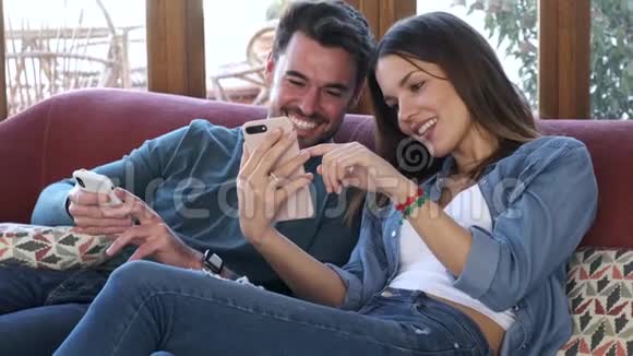 可爱的年轻夫妇在家里坐在沙发上用手机视频的预览图
