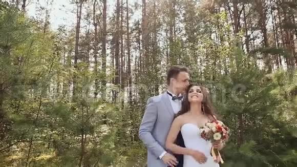 新娘和新郎在森林里摆姿势新郎亲吻拥抱新娘一对恩爱夫妻的幸福时刻视频的预览图
