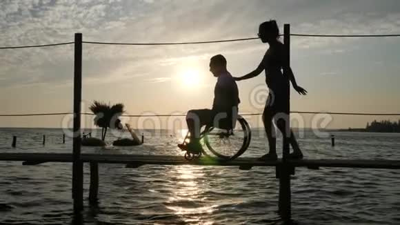 在日落时分身材匀称的女性和一个残疾的男子坐在轮椅上逆天视频的预览图