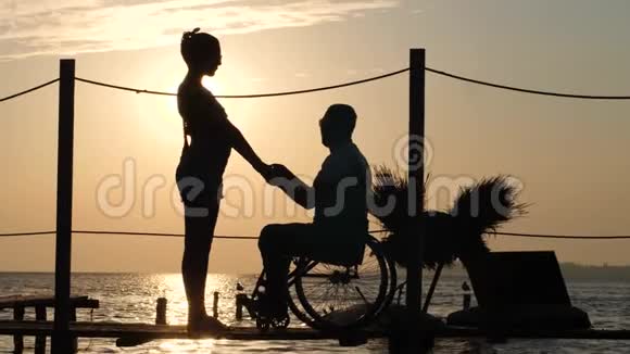 残男的剪影与心爱的女子在海上码头的傍晚余晖在橘色的天空和水的背景下视频的预览图