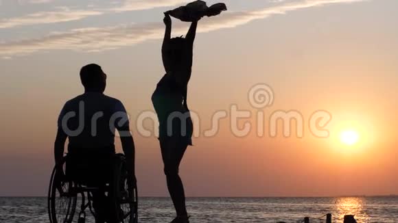 长腿女人站在码头上在坐轮椅的残疾人面前挥舞着一块布视频的预览图