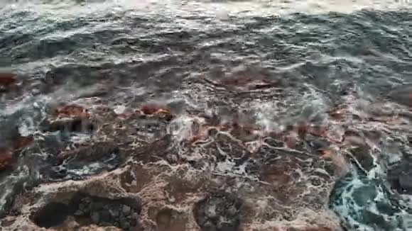 海浪撞击岩石海岸飞溅和创造白色泡沫的空中视图塞浦路斯日落时的落基海滩视频的预览图