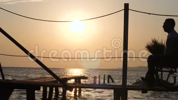 坐在轮椅上享受夏日海上日落的男人剪影视频的预览图