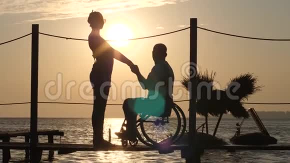 坐在轮椅上的男性和女性残疾人手挽手看着大海的地平线视频的预览图