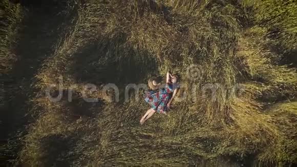 空中飞行一个穿着鲜艳裙子躺在干草堆里的年轻女人与自然宁静相统一的理念看法视频的预览图
