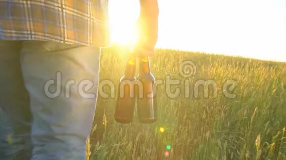 一个人走在麦田里在炎热的日子里带着两瓶啤酒日落时分太阳透镜耀斑慢镜头特写视频的预览图