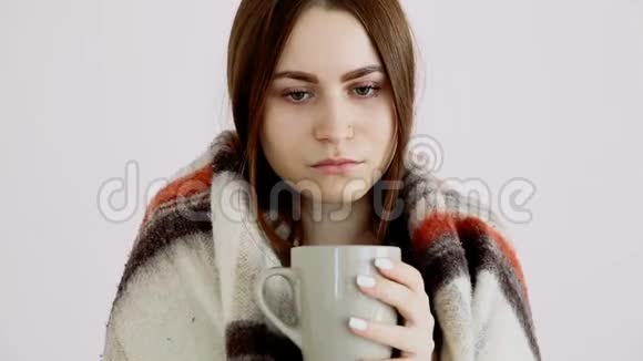 一个美丽的冷姑娘穿着羊毛毯在白墙边喝着热茶视频的预览图