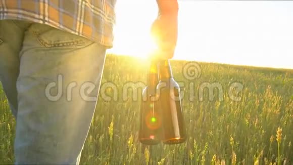 一个人走在麦田里在炎热的日子里带着两瓶啤酒日落时分太阳透镜耀斑慢镜头特写视频的预览图