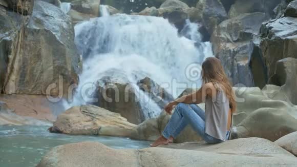 赤足女孩的啜泣和看岩石上的瀑布视频的预览图