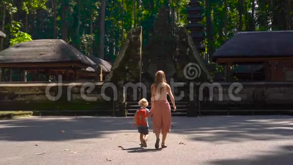 一名年轻女子和她的儿子在印度尼西亚巴厘岛的桑格猴子森林里行走的慢镜头视频的预览图