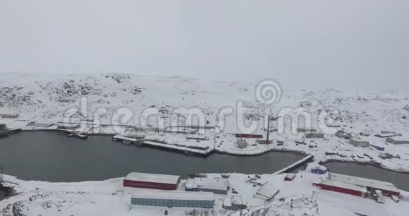 在灰色的天空下在未冻结的海水湾的低雪丘陵和房屋视频的预览图