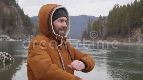 年轻的帅哥在寒冷的天气里站在山河的岸边慢动作视频的预览图